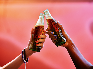 Global Coca-Cola Real Magic Cheers 2 Arms Glass Bottles on Pink Background.png